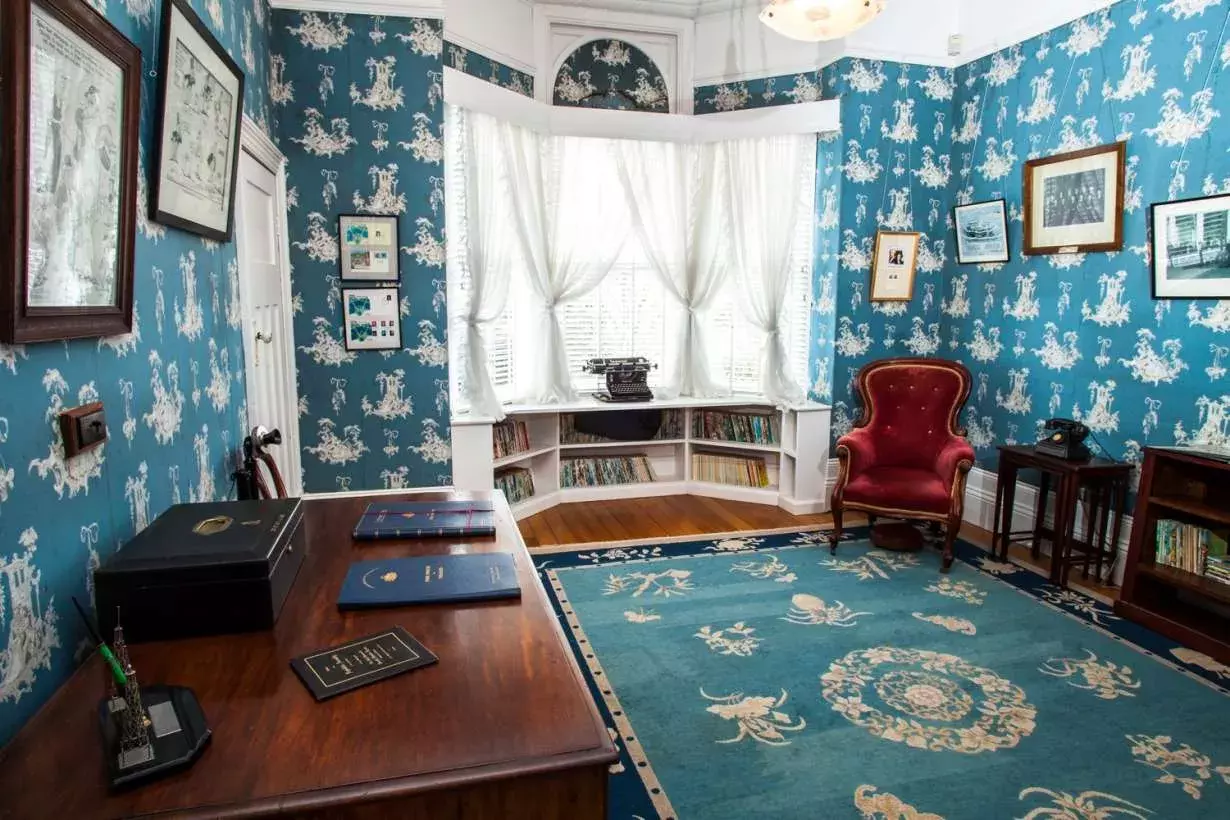 The office at Home Hill with vivid blue wallpaper, a bay window, timber furniture, blue carpet and pictures on the walls.  