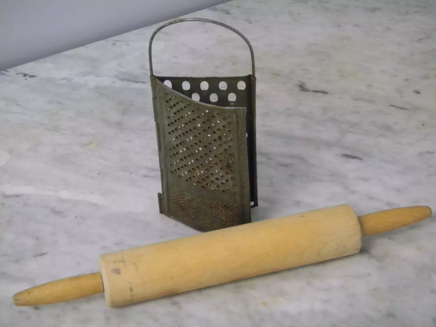 An old grater and a rolling pin on a kitchen bench.  