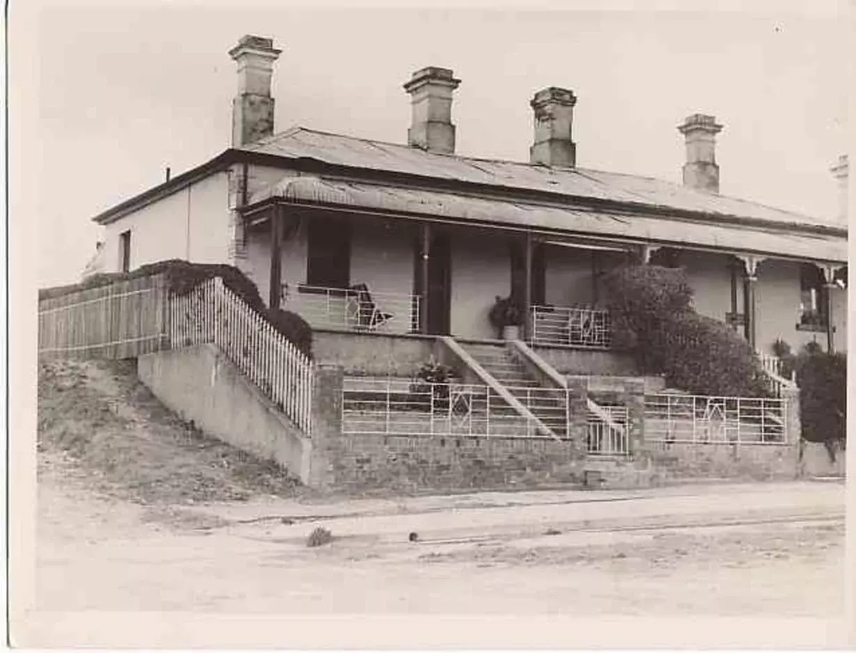 A black and white photo of Chifley's home at 10 and 12 Busby Street with a front verandah, four chimneys and a white metal fence with small art deco features.   