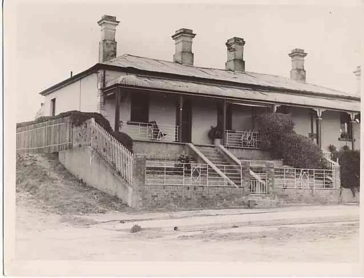 A black and white photo of Chifley's home at 10 and 12 Busby Street with a front verandah, four chimneys and a white metal fence with small art deco features.