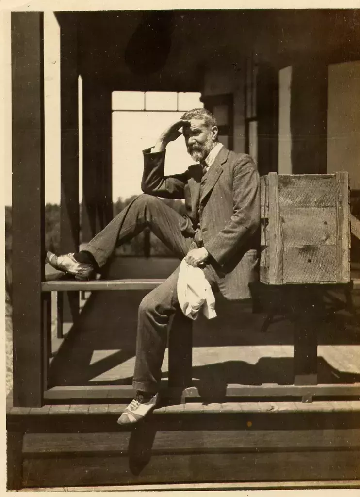 Alfred Deakin sitting on the edge of a porch with one leg up, looking out.  
