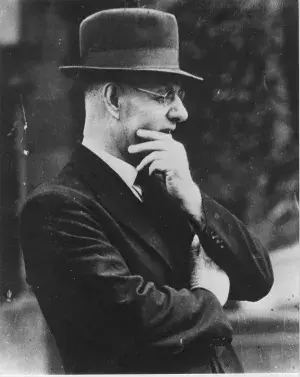 Black and white photo of John Curtin wearing a hat with his hand on his chin.  
