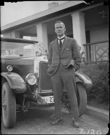 Black and white photo of Mildenhall standing in front of an automobile.  