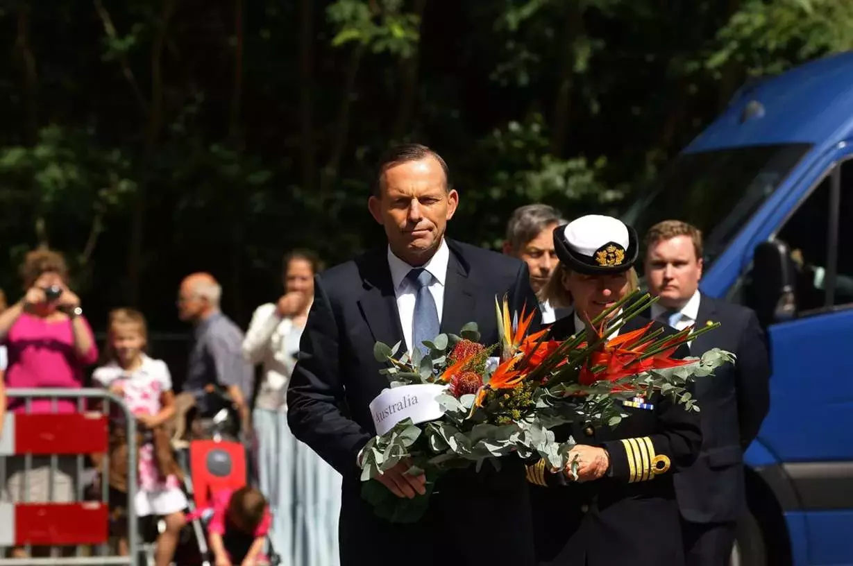 Tony Abbott carries flowers at a memorial.
