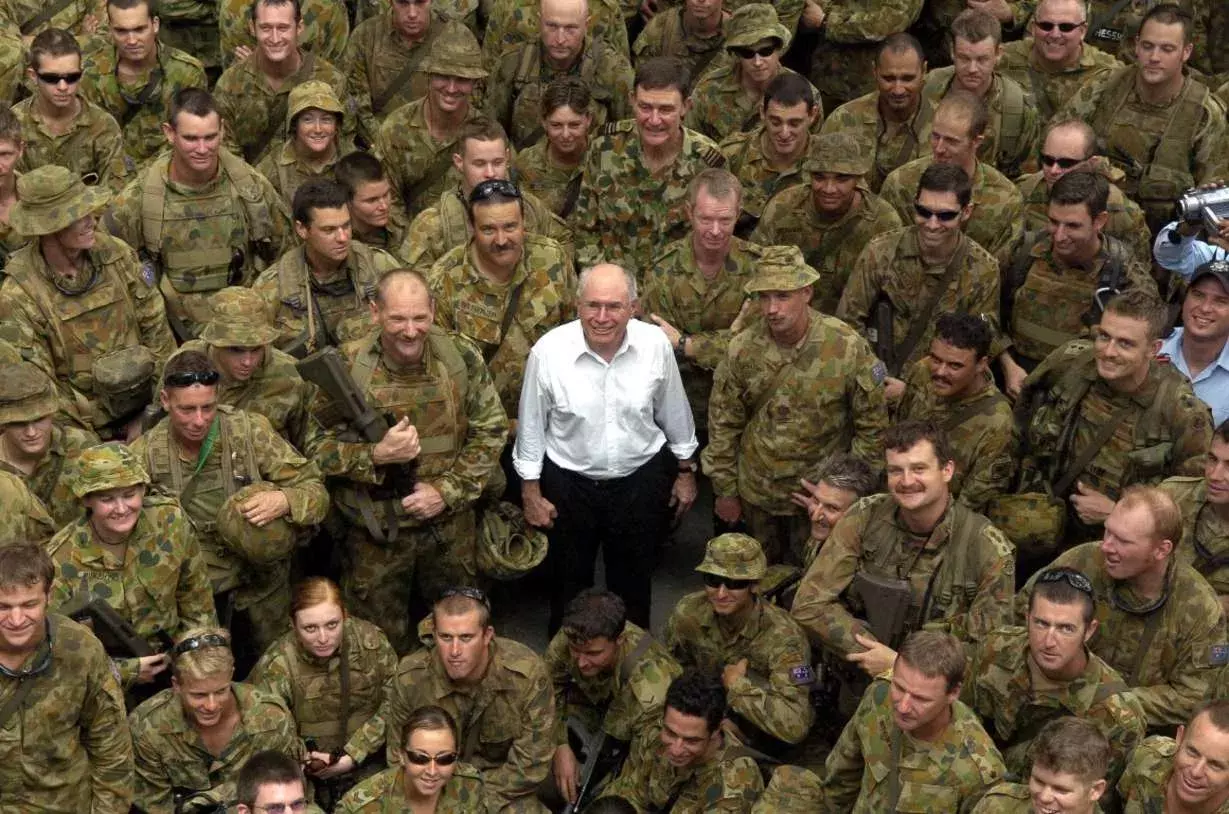 John Howard stands in the middle of a large crowd of soldiers.  