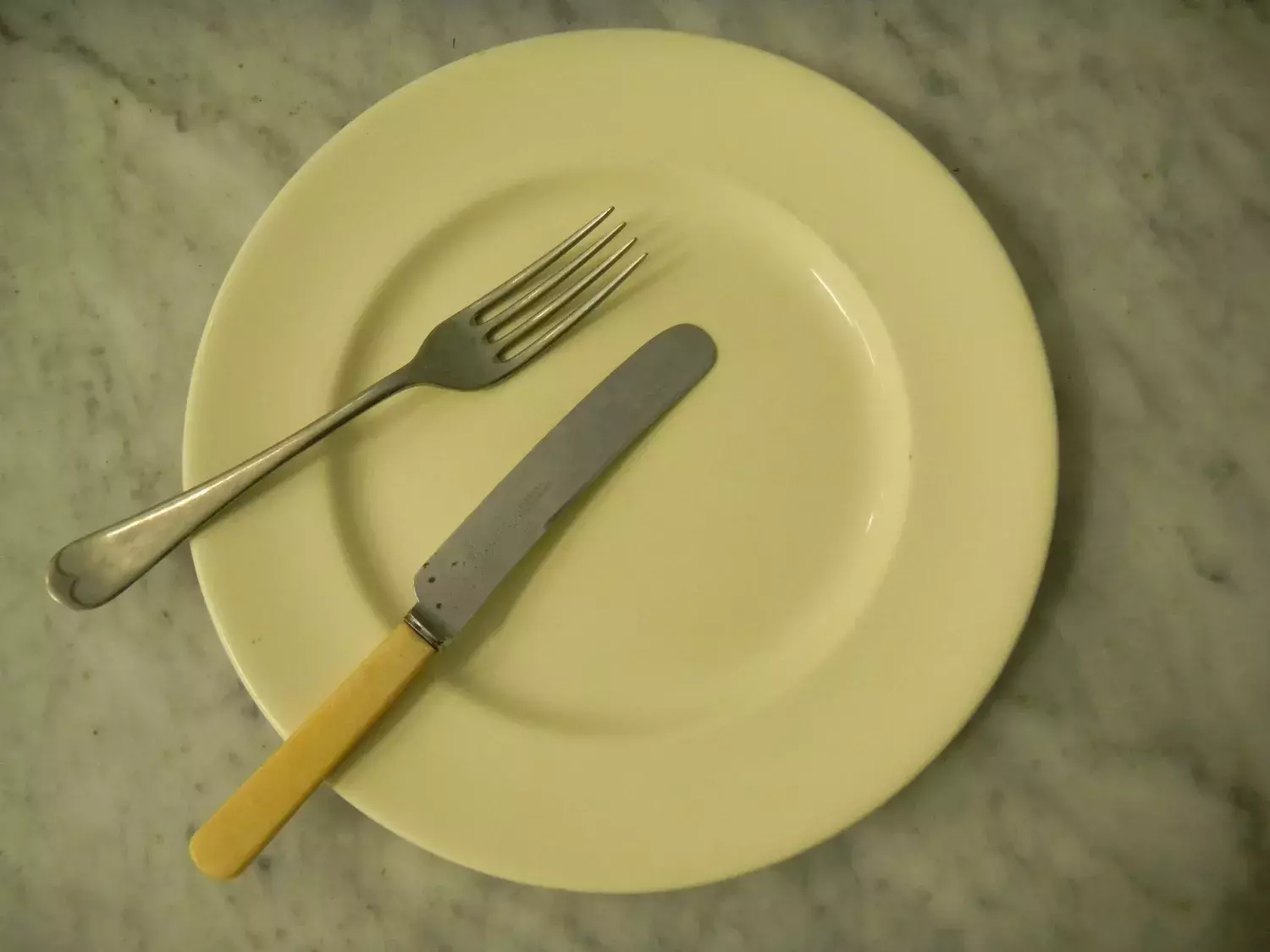 A yellow plate with a knife and fork on top of it.  